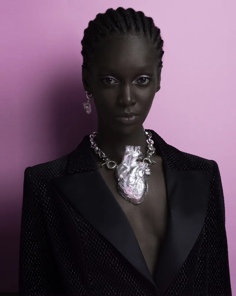 Modelo de frente con blazer negro y un collar de plata sobre fondo lila